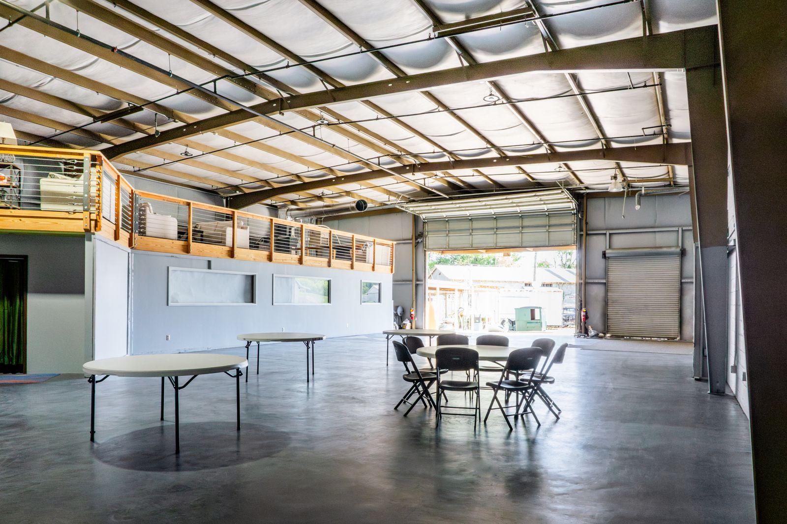 Big Room set with a round table and chairs, loft railing above and tall windows