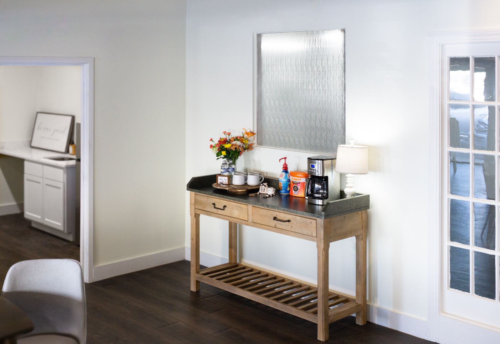 Console styled with fresh flowers, a lamp, and refreshments against a white wall