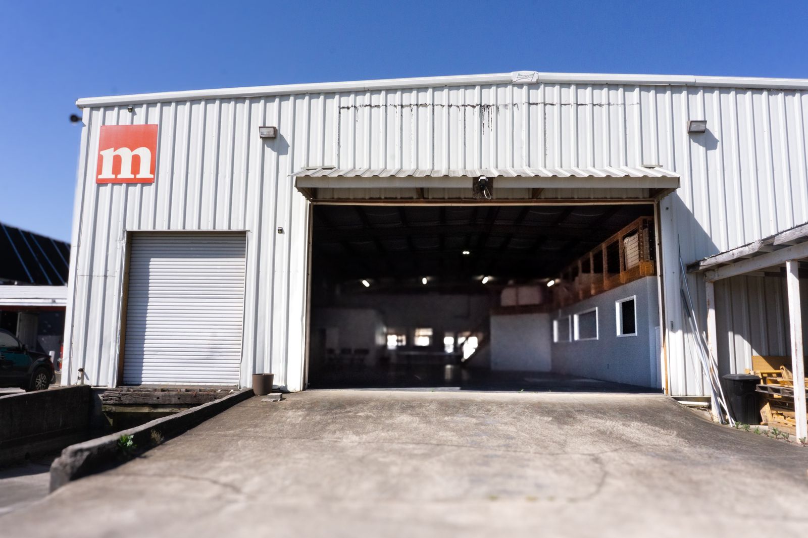 Wide exterior of the venue's white metal event building with its roll-up door open